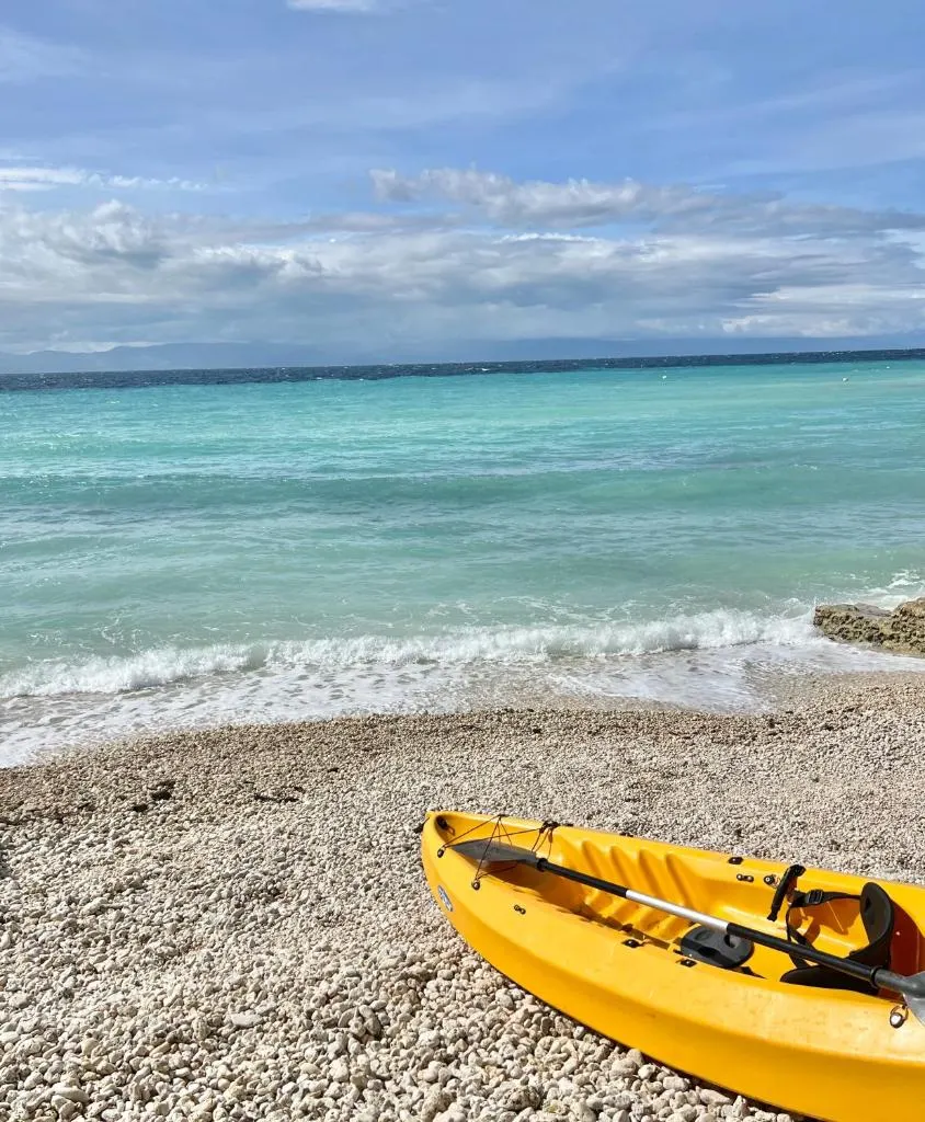 Clear turquoise water and a pebble beach with a yellow kayak
