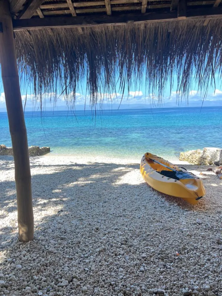 A kayak on the beach seen from under a thatched shade